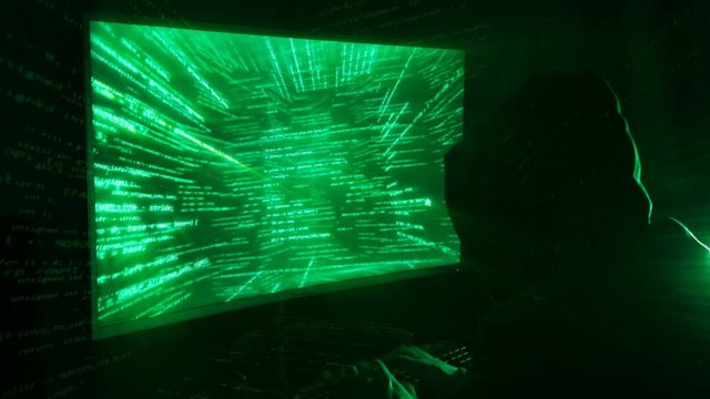 A man hacker in a hood in a dark room works with the program code