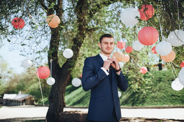 Happy groom corrects a tie and smiles gladly. A wedding walk in the summer park. Wedding concept.