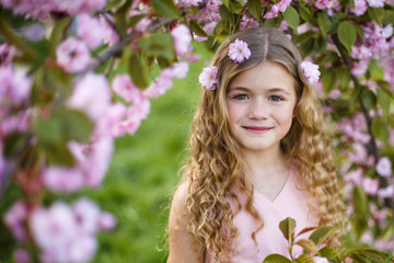 Pretty little girl in blossom cherry garden in sunny spring day