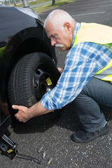 Fototapeta na wymiar aged man changing leaking tire on the verge