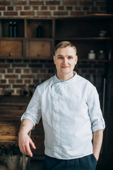 Portrait of a charismatic chef with blue eyes who stands in the kitchen in a white uniform