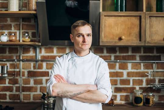 Portrait of a handsome chef with blue eyes who stands in the kitchen in a white uniform
