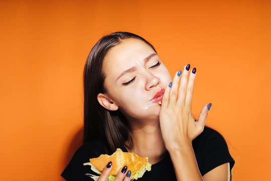 hungry woman on an orange background eating a sandwich