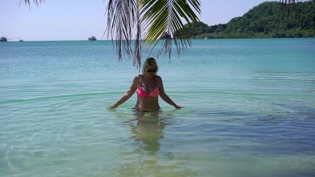 Young woman in pink bikini at the beach walking near palm