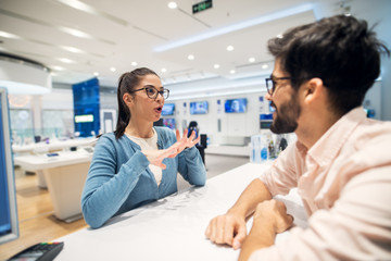 Beautiful young brunette talking with employe in the tech store.