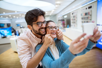 Lovely cheerful hipster multiracial couple in the tech store taking a selfie with the shop phone.