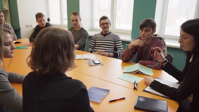 Teacher sits at a table and talks with students at university