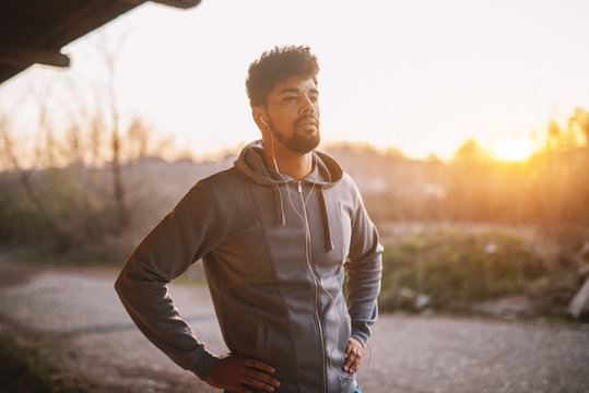 Portrait of focused motivated afro-american young handsome sportive man with earphones standing outside at sunset. Successful young active man portrait.