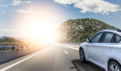 A white car rushing along a high-speed highway in the sun.