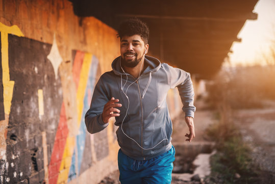 Portrait of active motivated afro-american young attractive athletic man with earphones running inside of the abandoned place.