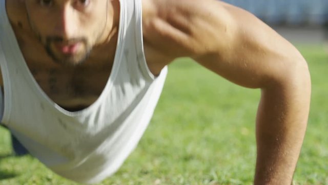 Camera pans across a man doing push ups outdoors, in slow motion