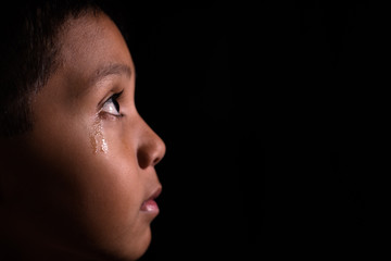 young asian boy looking into light in darkness with tears in his eye. emotion and expression concept.