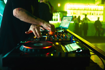 Close up view of the hands of a male disc jockey mixing music on his deck with his hands poised over the vinyl record on the turntable and the control switches at night