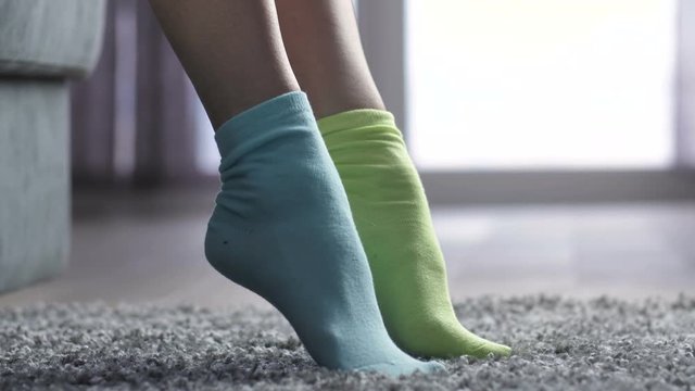 Close-up of female feet on the carpet, woman putting on different colored socks. Uniqueness, difference and independance concept. Side view