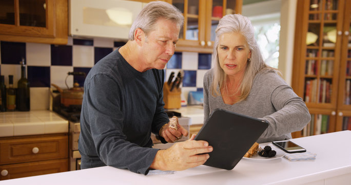 Charming mature white couple looking at handheld tech while eating lunch