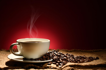 Cup of coffee with smoke and coffee beans on reddish brown background