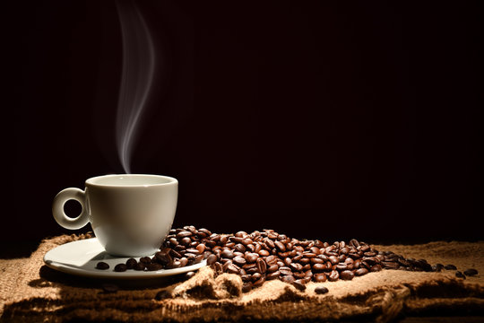 Fototapeta Cup of coffee with smoke and coffee beans on black background