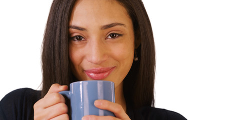A close-up portrait of a Hispanic woman drinking coffee on a white background. A Latina looks at the camera on a blank backdrop
