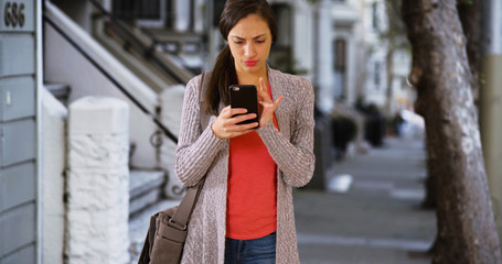 A Hispanic millennial uses her smart phone to call a ride share. A Latina uses her mobile phone to call a taxi