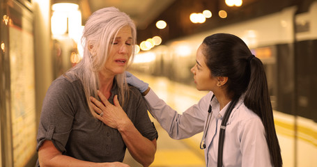 An EMT helps a sick woman at a train station. A woman in pain is helped by a medical professional