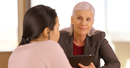 A smiling business executive has a meeting with her employee. An older office worker with a tablet meets with an employee