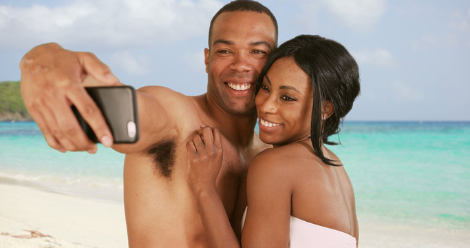Engaged couple on honeymoon taking selfies on Caribbean beach. Man and woman with smartphone being silly and playful