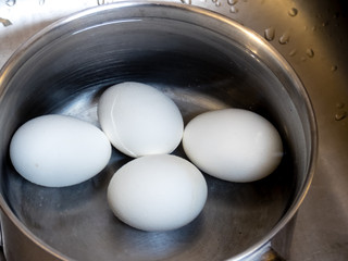 Four boiled eggs in a pot of water. One egg is cracked.