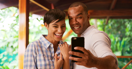 A black couple takes a selfie to celebrate their engagement. An African American man and woman take a picture using a smart phone of her new wedding ring