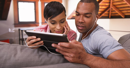 A black man and woman listen to music on their tablet. An African American couple listen on their pad