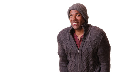 An African American man stands trembling on a white background. A black guy poses in his winter outfit on a blank backdrop