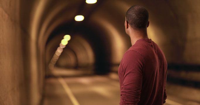 African American stares down a tunnel. A black man looks for a light at the end of the tunnel