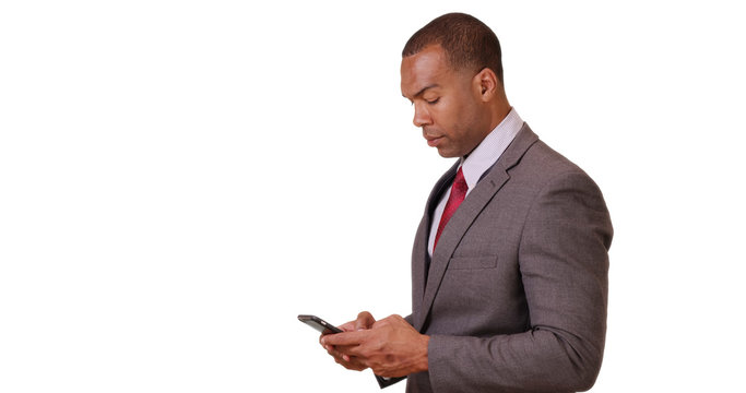 An African American businessman crosses his arms and then looks at his smart phone on white background. A black executive uses his mobile phone for work on a blank backdrop