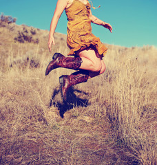 pretty woman in a skirt jumping up in cowboy boots in a wheat field on a hot summer day toned with...