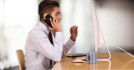 Hispanic business man working on computer while talking on cellphone. Mexican businessman making...