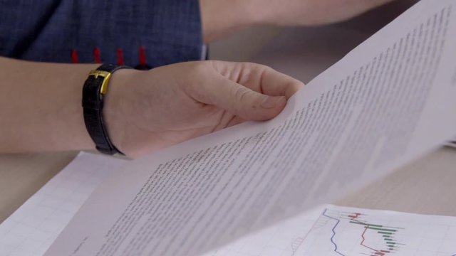 Close-up of person is study important document with text with pen in hands. Specialist reads on paper an analytical note to schedule of stock quotes, bitcoin, and crypto currency in foreign exchange