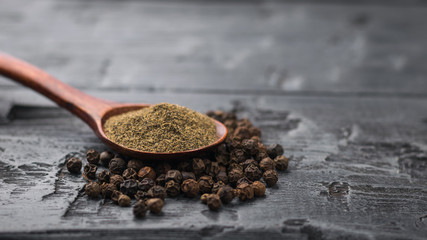 A wooden spoon with ground black pepper on a pile of whole pepper on a wooden table.