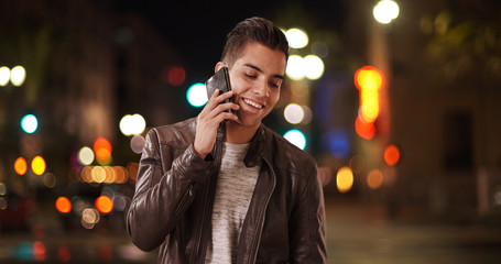 Millennial Latino man receiving cell phone call on city street at night. Hispanic guy using...