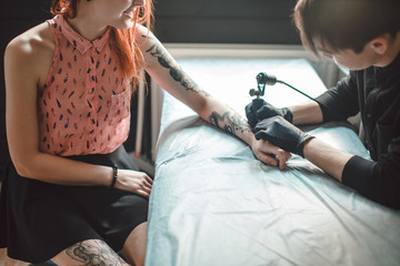 Tattoo is art. Pretty girl getting a tattoo. Image of the bearded tattoo male artist makes a tattoo...