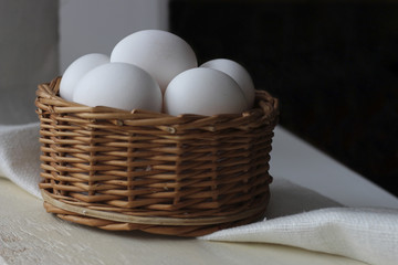 White chicken eggs in a wicker basket are on the table.
