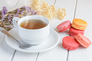 Different types color of macaroons with Cup of hot tea on white wooden background