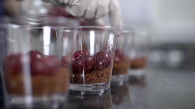 Cherries are being put to the glass baking forms, close up. Female confectioner is using her hand to spread berries into the containers with chocolate dough at the buttom, which are standing in a row
