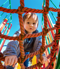 Multracial toddler boy climbing on a playground ropes