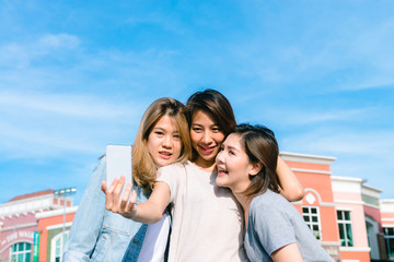 Group of young Asian Women selfie themselves with a phone in a pastel town after shopping. Young women group do outdoor activity under the blue sky. Outdoor activity after shopping concept.