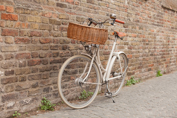 Fototapeta na wymiar White bike with basket standing near brick wall in Brugge,