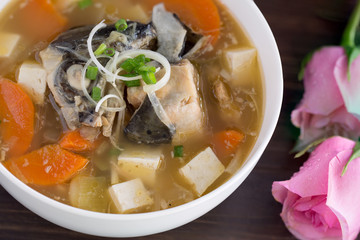 Japanese soup hot (Miso) with head salmon in white bowl on brown wooden table, Decoration with pink rose