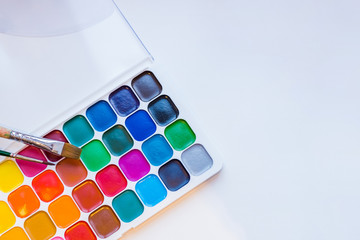 Tools for creative work on a white wooden background. Watercolor paintbox. Color paints with paint...