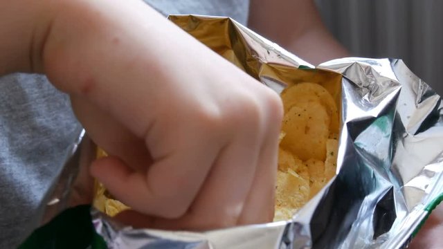 Teenager boy eats potato chips from a package. Unhealthy food, fast food