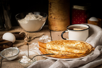 Stack of crepes and ingredients for cooking on a table.