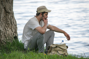 young man is resting near a tree on the river Bank