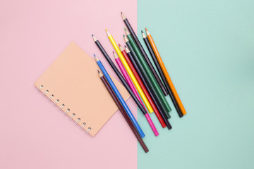 Color pencils and notebook on a colored background, top view